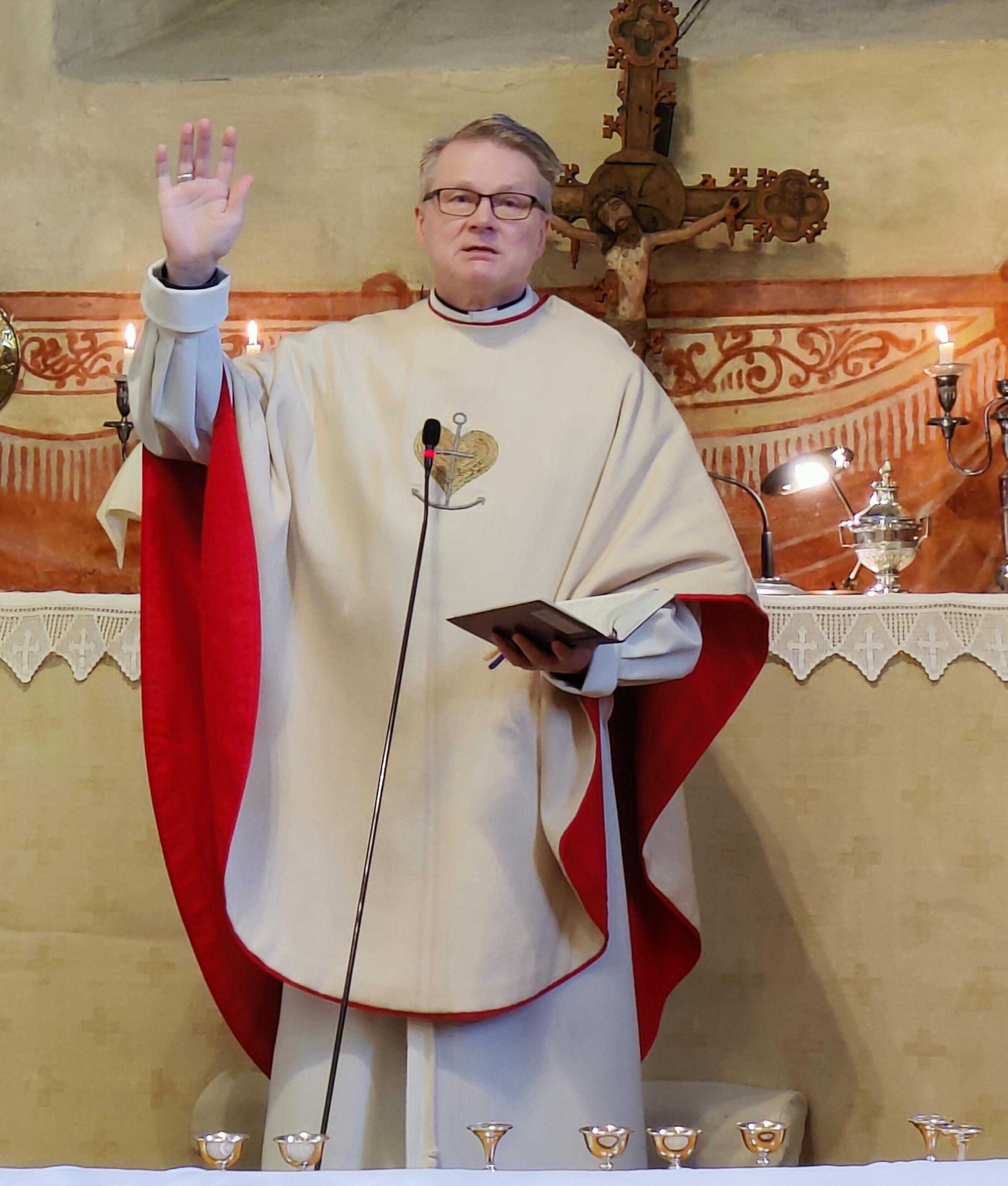 Pappi kirkon alttarilla käsi kohotettuna siunaukseen.